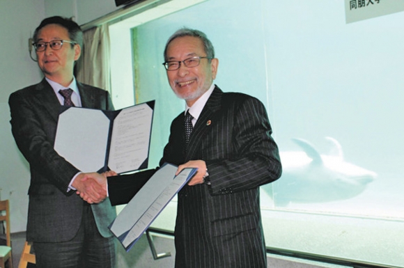 イルカに見守られながら協定書を交わす松田学長（右）と鷲見社長＝美浜町の南知多ビーチランドで