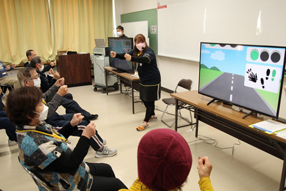 画面に映る信号の色の変化に合わせて手足を動かす実証実験の参加者＝昨年１１月、三重県鈴鹿市内で