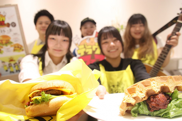 ヤンニョムチキンを使ったワッフルバーガー（右）などをＰＲする学生ら＝北区名城２で