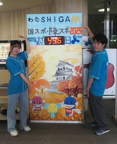 カウントダウンボードをＰＲする仲地さん（左）、青山さん＝長浜市田村町の長浜バイオ大学ドームで
