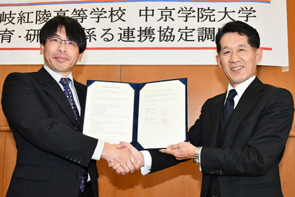 協定書を持ち握手を交わす中京学院大の林学長（右）と土岐紅陵高の田中校長＝土岐市下石町の土岐紅陵高で
