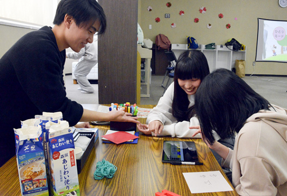 タブレット端末で算数ゲームを解く利用者に教える井上輝星さん（左）ら＝内灘町向粟崎のキッズステーションうちなだで