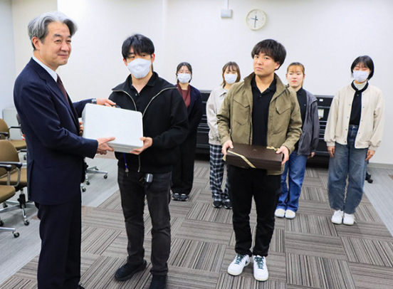 吉村光輝町長（左）に義援金を手渡す学生たち＝穴水町役場で