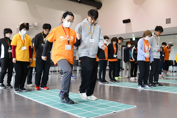 学生たちと升目の上を歩いて運動するヘルスサポートリーダー＝豊田市貝津町で