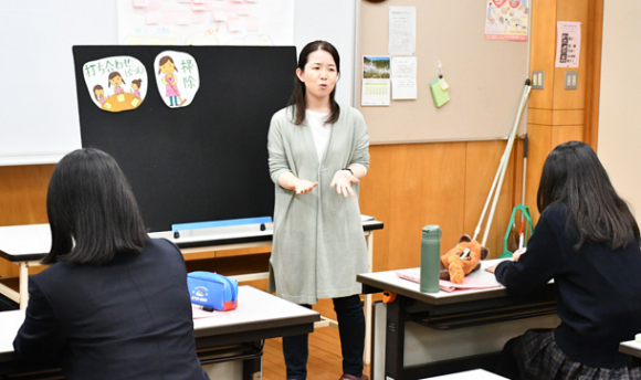 栗岡准教授から保育者の一日の流れを教わる生徒たち＝土岐市下石町の土岐紅陵高で