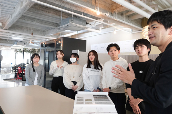 社員（右）からオフィスのこだわりについて教わる学生ら＝中区の丸天産業で