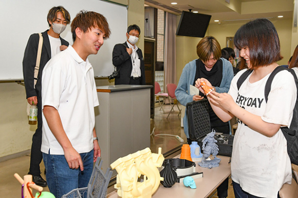 3Dプリンターで作った造形物を学生に紹介する富田社長(左)=岐阜市中鶉の岐阜聖徳学園大で