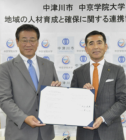 協定書にサインを交わした中谷理事長（左）と小栗市長＝中津川市役所で