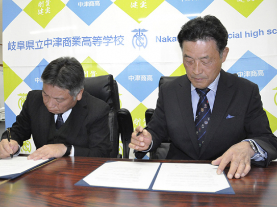 協定書にサインする丸山校長(左)と石川学長=中津川市の中津商業高で