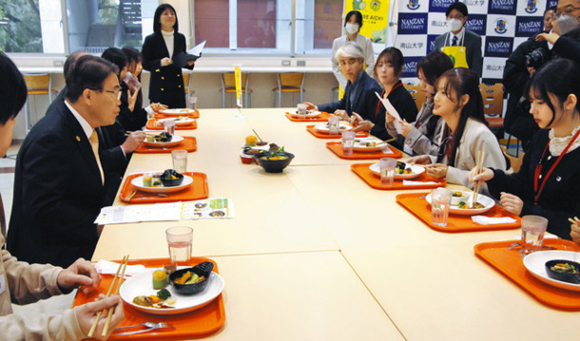 学食メニューを試食しながら大村知事(左端)と懇談する学生=名古屋市昭和区の南山大で