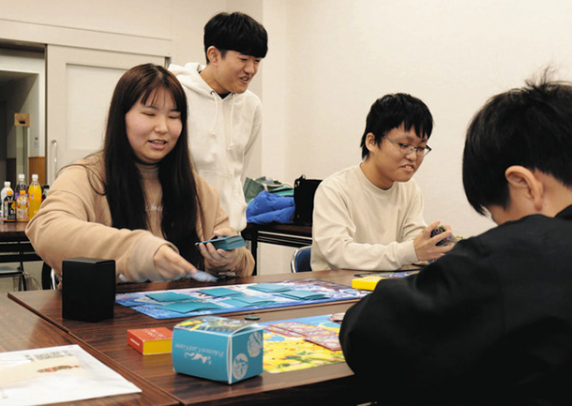 参加した小学生(手前)とカードゲームで遊ぶ、(左から)辻さん、大嶋さん、小倉さん=松阪市殿町の市福祉会館で