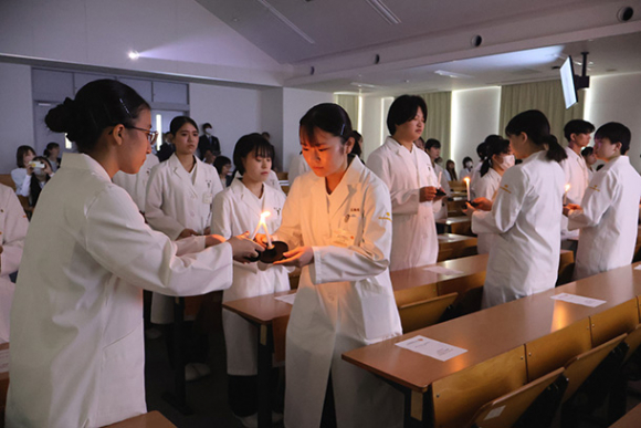 ろうそくの明かりをつなぐ学生たち=四日市市の四日市看護医療大で