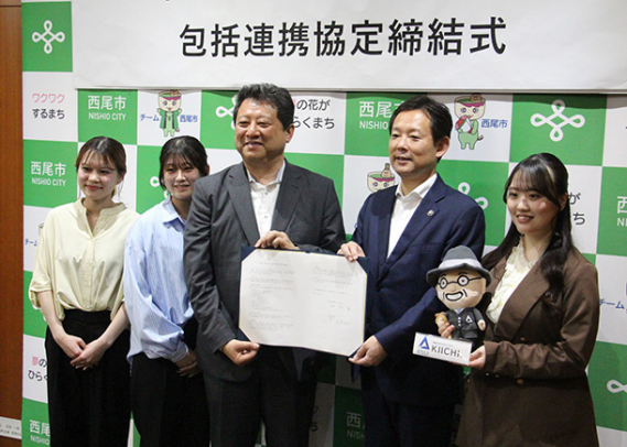 協定書を手にする中村市長(右から2人目)と広瀬学長(同3人目)。学生が持つぬいぐるみは愛知大創業者を模したキャラクターKIICHI(キイチ)くん=西尾市役所で
