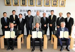 協定書を掲げる（下段左から）松田校長、加来教育長、児玉学長ら＝半田市役所で