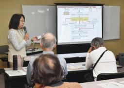 患者がテレビ番組やＣＭの影響を受けていると指摘する半谷准教授（左）＝日進市民会館で