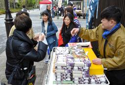 五百円市で店主(右)と一緒に笑顔で接客する学生ら=中区栄1で