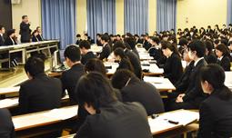 担当者(左)の事業概要の説明を聞く学生たち=美浜町の日本福祉大美浜キャンパスで