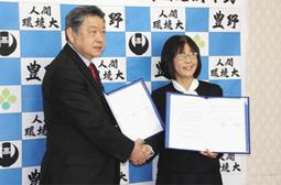 協定書を手に握手を交わす豊野高の大石校長（右）と人間環境大の牧山学長＝豊田市渡刈町の同高で