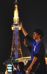 「世界自閉症啓発デー」に合わせ、青色にライトアップされたテレビ塔を背に、啓発イベントで手を振る中京大の学生ら=中区のもちの木広場で