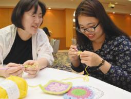 会員と会話を楽しみながらアクリルたわしを編む留学生（右）＝大垣市の大垣フォーラムホテルで