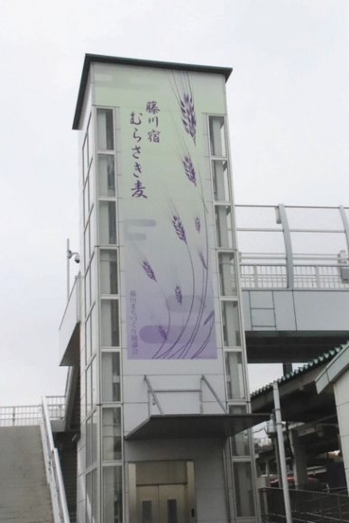 藤川駅エレベーター棟の壁面に飾られたむらさき麦のＰＲパネル＝名鉄藤川駅で